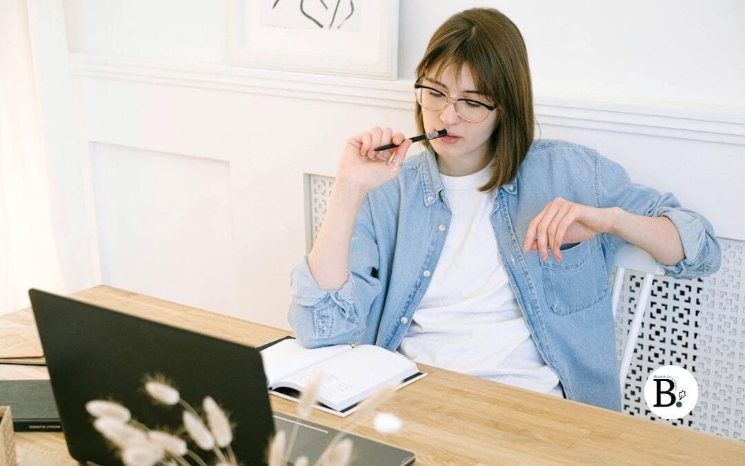 Femme cheveux mi-longs avec un crayon au coin de la bouche qui réfléchit