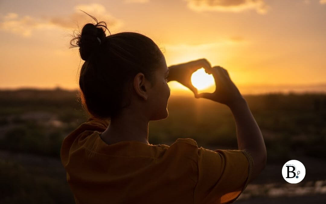 Femme qui fait un cœur avec ses mains en entourant le soleil