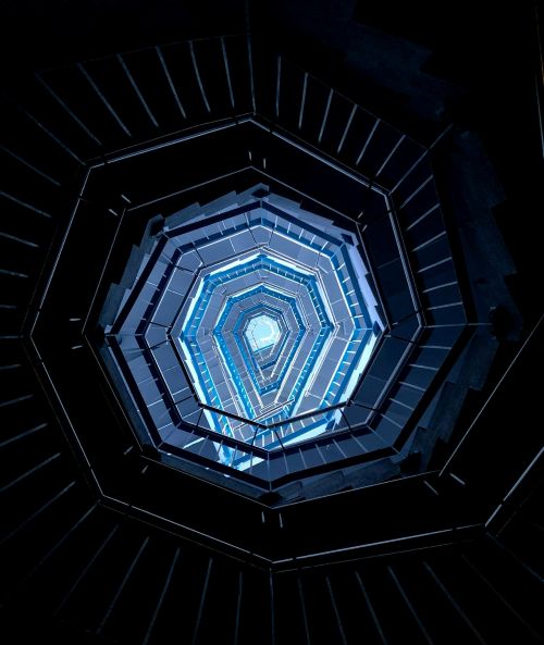 Photographie en contre-plongée d'un escalier moderne. Les rampes et les marches forment des lignes diagonales de fuite marquées, éclairées par un dégradé de lumière bleue sur un fond noir contrasté. Les 3 types de lignes en photo : réussir vos clichés