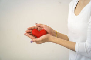 Femme avec un teeshirt blanc qui tient un coeur rouge entre ses mains.