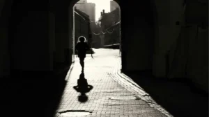 Photo en noir et blanc d'une femme qui avance dans une ruelle à contre-jour