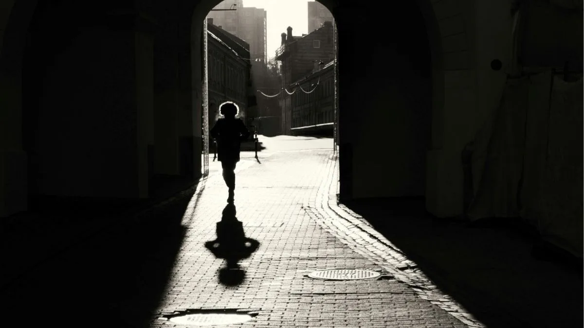 Photo en noir et blanc d'une femme qui avance dans une ruelle à contre-jour