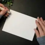 Mains d'une femme qui tient une feuille blanche et un stylo blanc dans sa main gauche