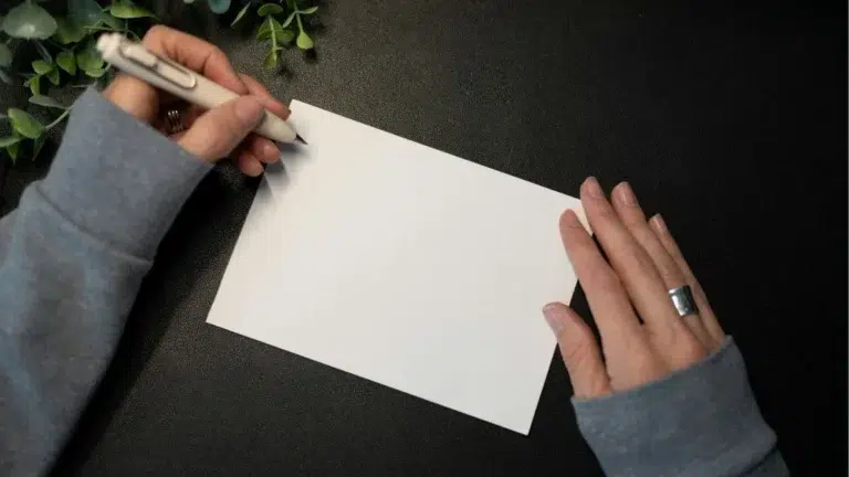 Mains d'une femme qui tient une feuille blanche et un stylo blanc dans sa main gauche