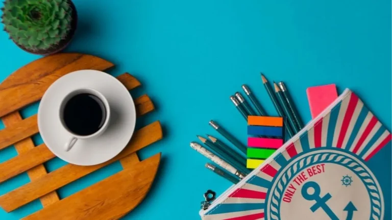 Trousse à crayons à motif d’ancre ouverte sur fond bleu, crayons et onglets colorés qui débordent, à côté d’une tasse de café sur un dessous de bois et d’un petit cactus.