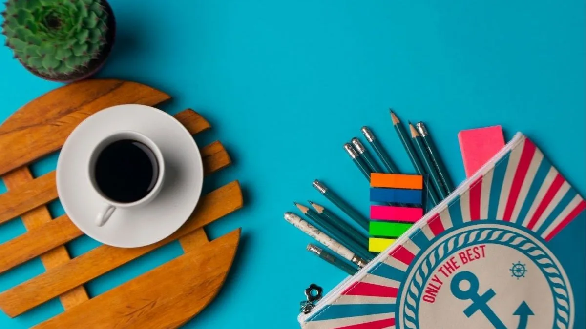 Trousse à crayons à motif d’ancre ouverte sur fond bleu, crayons et onglets colorés qui débordent, à côté d’une tasse de café sur un dessous de bois et d’un petit cactus.