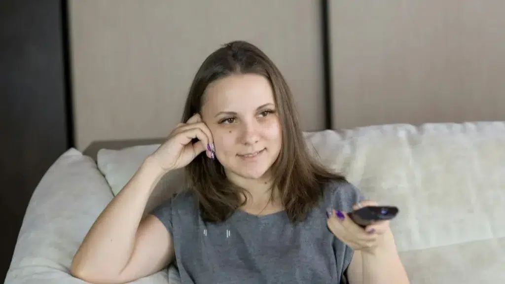 femme sourire assise canapé télécommande smart tv IPTV : combien d’écrans choisir pour votre foyer ?